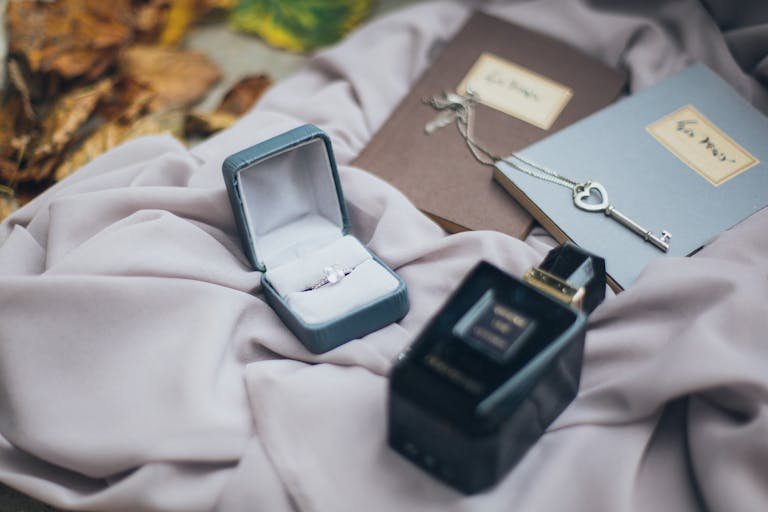 A romantic setup featuring a ring, vintage key ring, and perfume on soft fabric with autumn leaves.