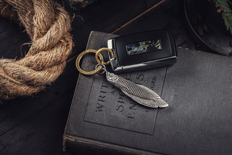 A stylish silver fish pendant key ring rests on an old English book with natural rope.