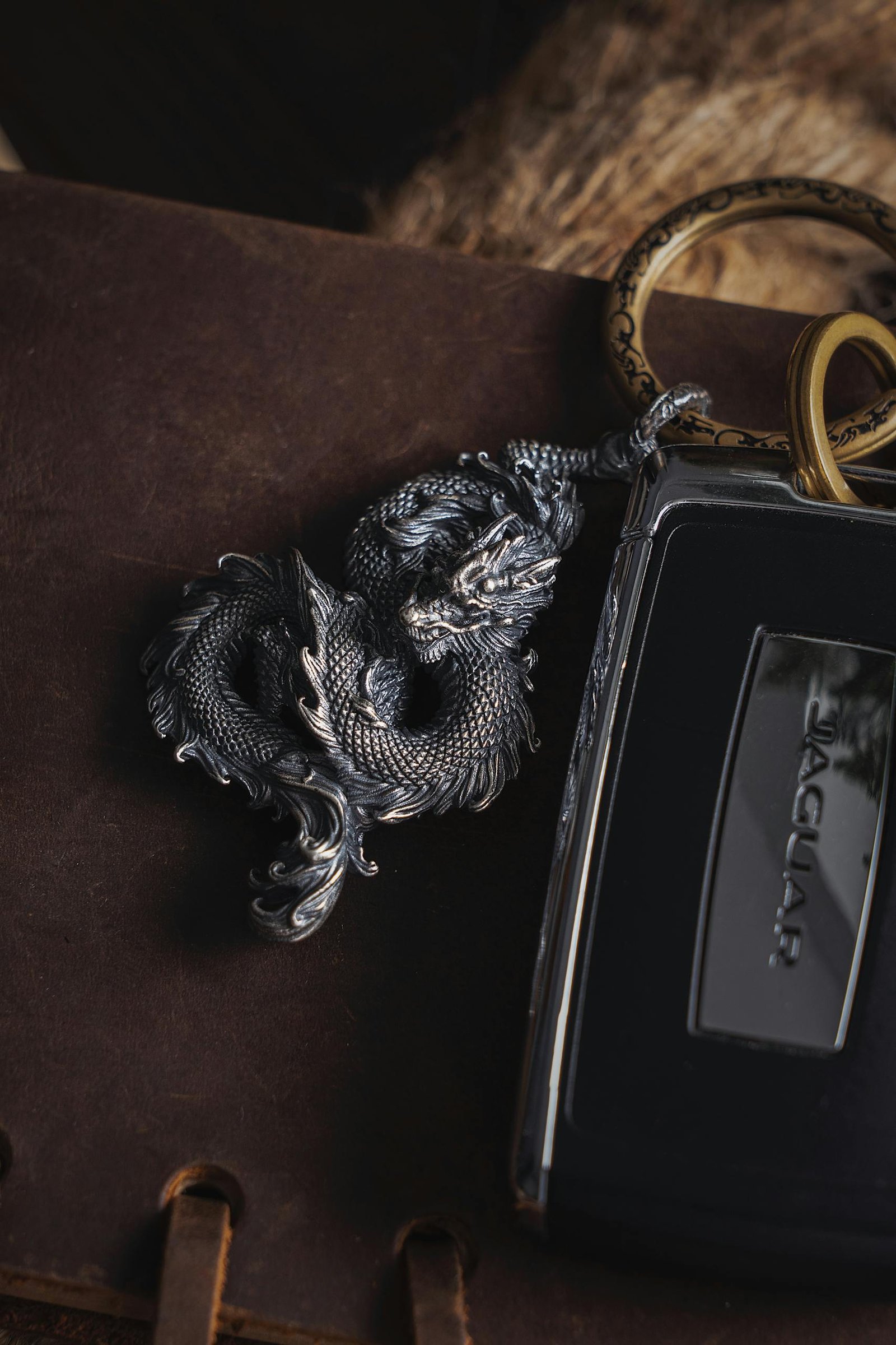 Close-up of a metallic dragon charm key ring paired with a luxury car key, showcasing elegance.