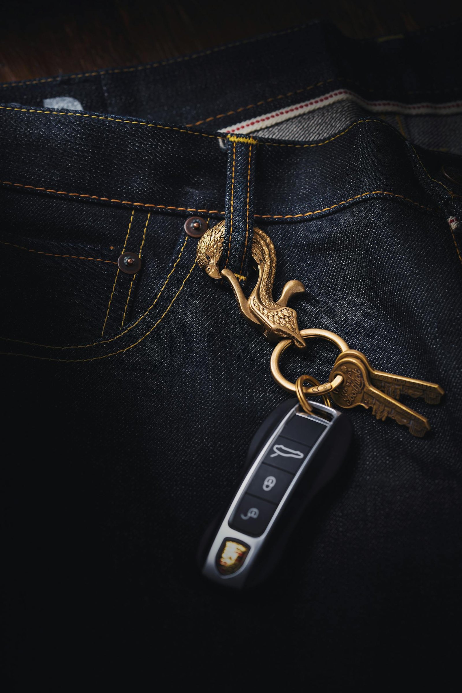 Detailed close-up of a car key and dragon keychain hanging on denim jeans.