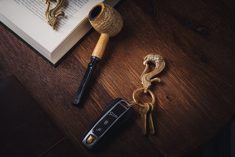 Elegant artistic arrangement of a key ring and pipe on a wooden surface with a book and keys.
